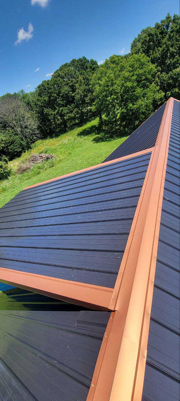 Close-up of a dark standing-seam metal roof panel edge with copper-colored trim, Dedicated Builders