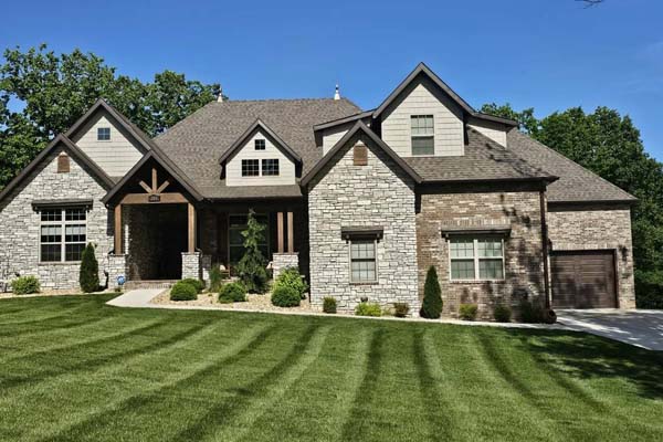 Finished stone-and-siding two-story home with brown shingles and a striped lawn, Dedicated Builders